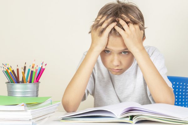 Upset schoolboy with pile of school books and notebooks