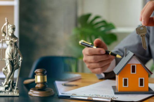 Judge holding wooden judge hammer against house background and businessman documents and house model on wooden table Real estate disputes and property auction concept